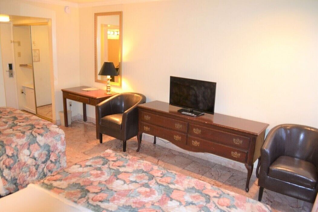 A hotel room with a bed, a desk, a chair, a television, and a dresser.