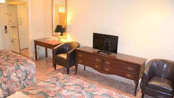 A hotel room with a bed, a desk, a chair, a television, and a dresser.