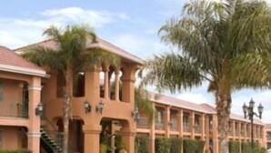 A hotel with a symmetrical facade, palm trees, and a central entrance with a staircase. - Merced Inn and Suites (Merced)
