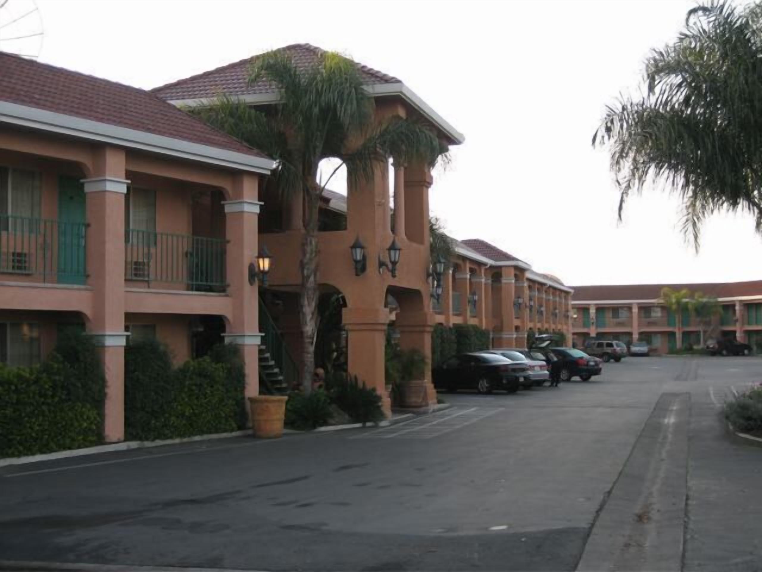 A hotel with a row of balconies, a central courtyard, and a parking lot.