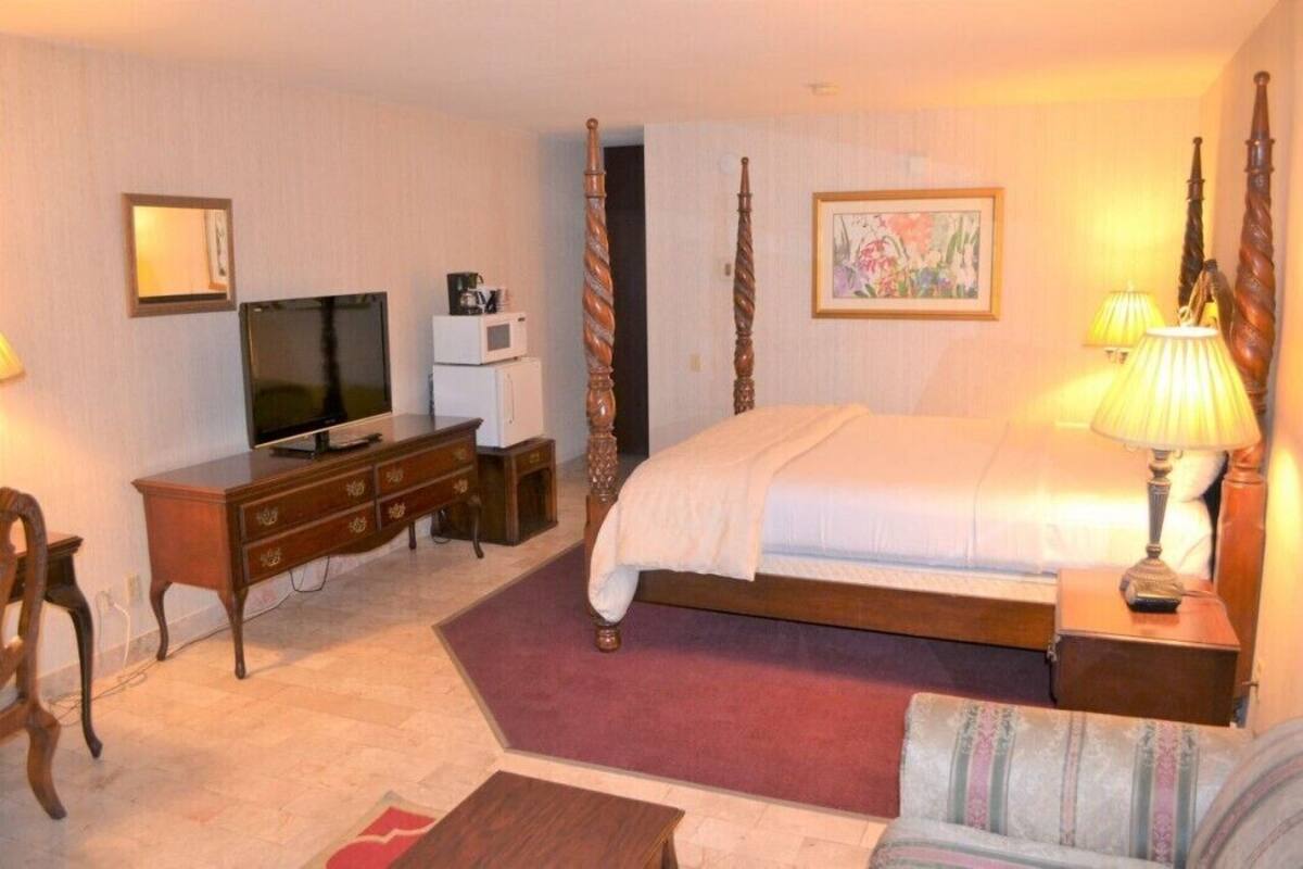 A hotel room with a bed, a TV, a desk, a chair, a lamp, and a painting on the wall.