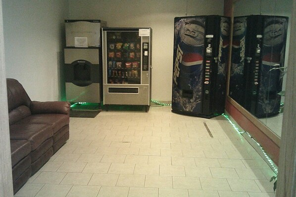 A room with a brown leather sofa, a vending machine, and a wall with Pepsi banners. - Rodeway Inn Roswell West (Roswell)