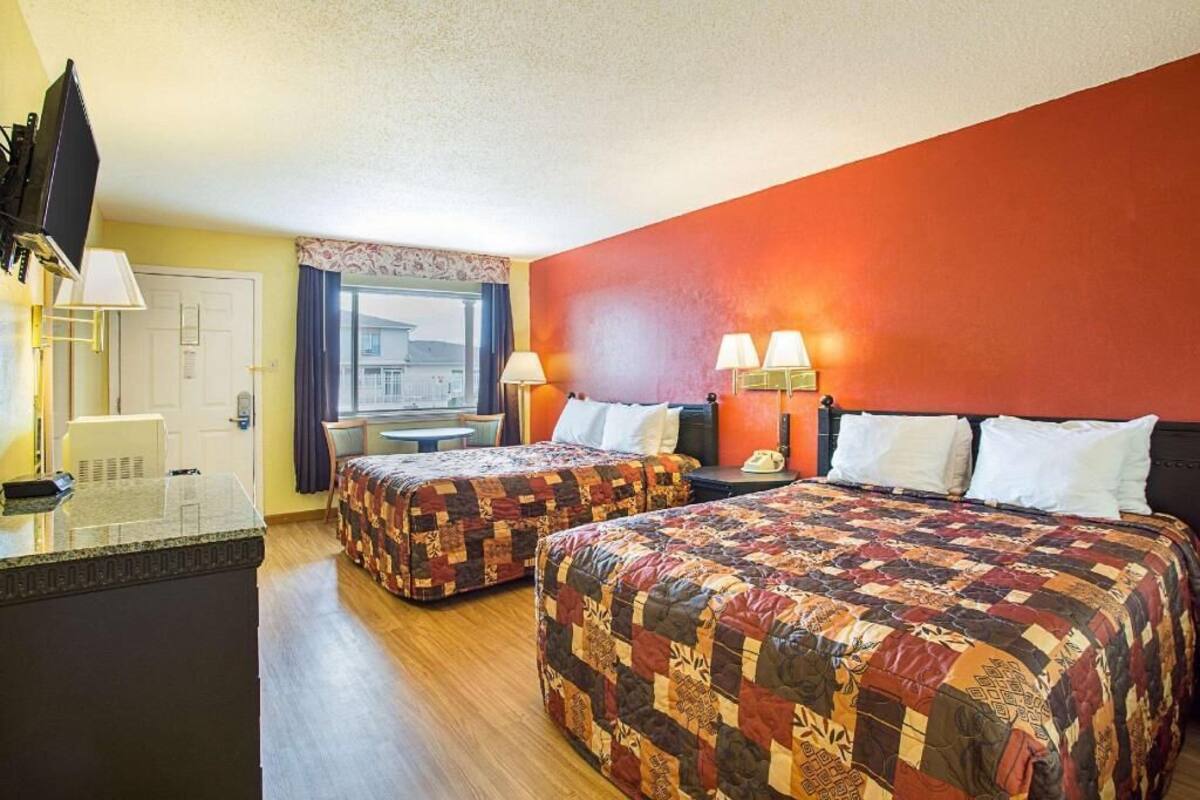 A hotel room with two beds, a desk, a TV, and a window with curtains.