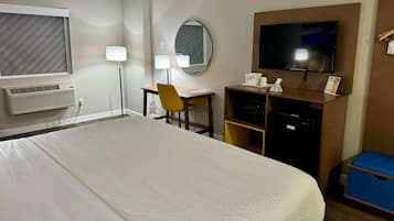 Habitación de hotel con una cama grande, un escritorio con silla, televisor, espejo y un minibar.