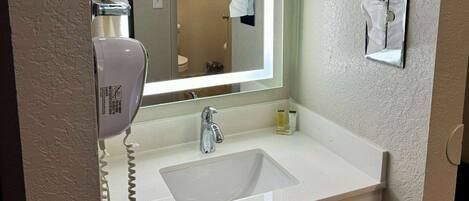 A bathroom with a white sink, a mirror, a towel dispenser, and a hand dryer.