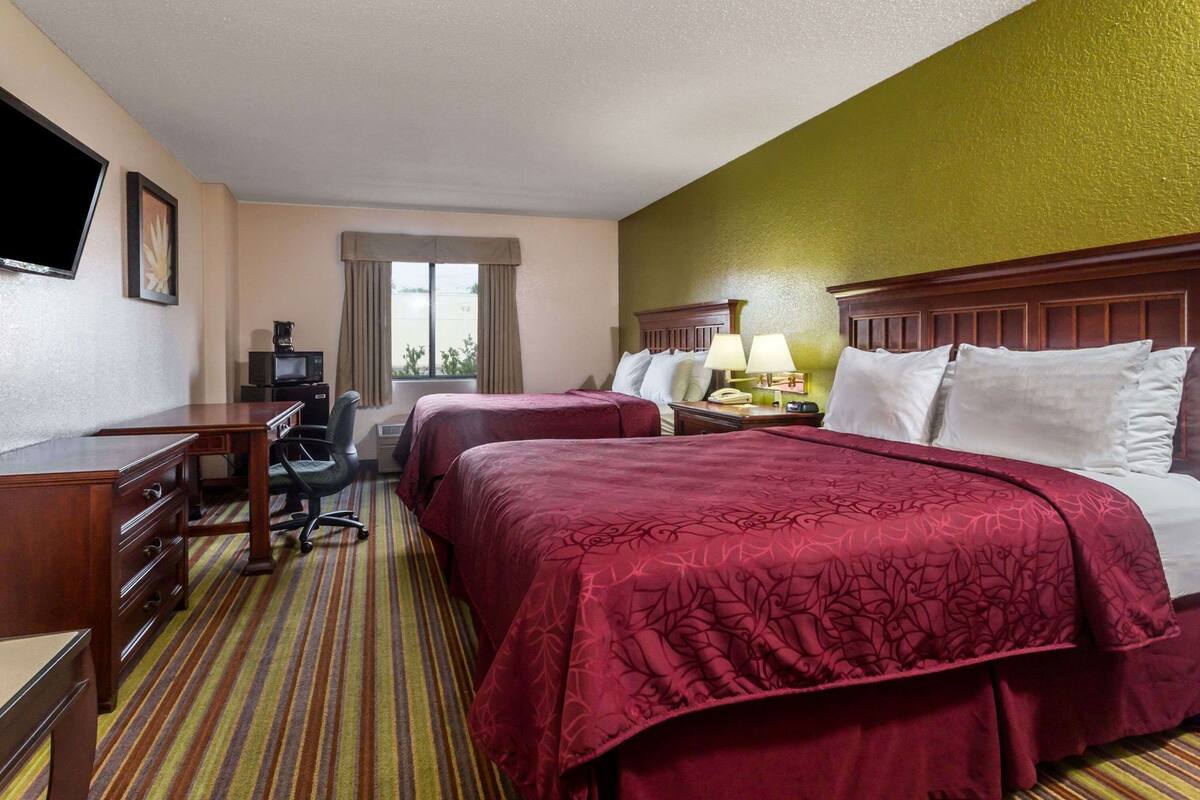A hotel room with two beds, a desk, a chair, a television, and a window with curtains.