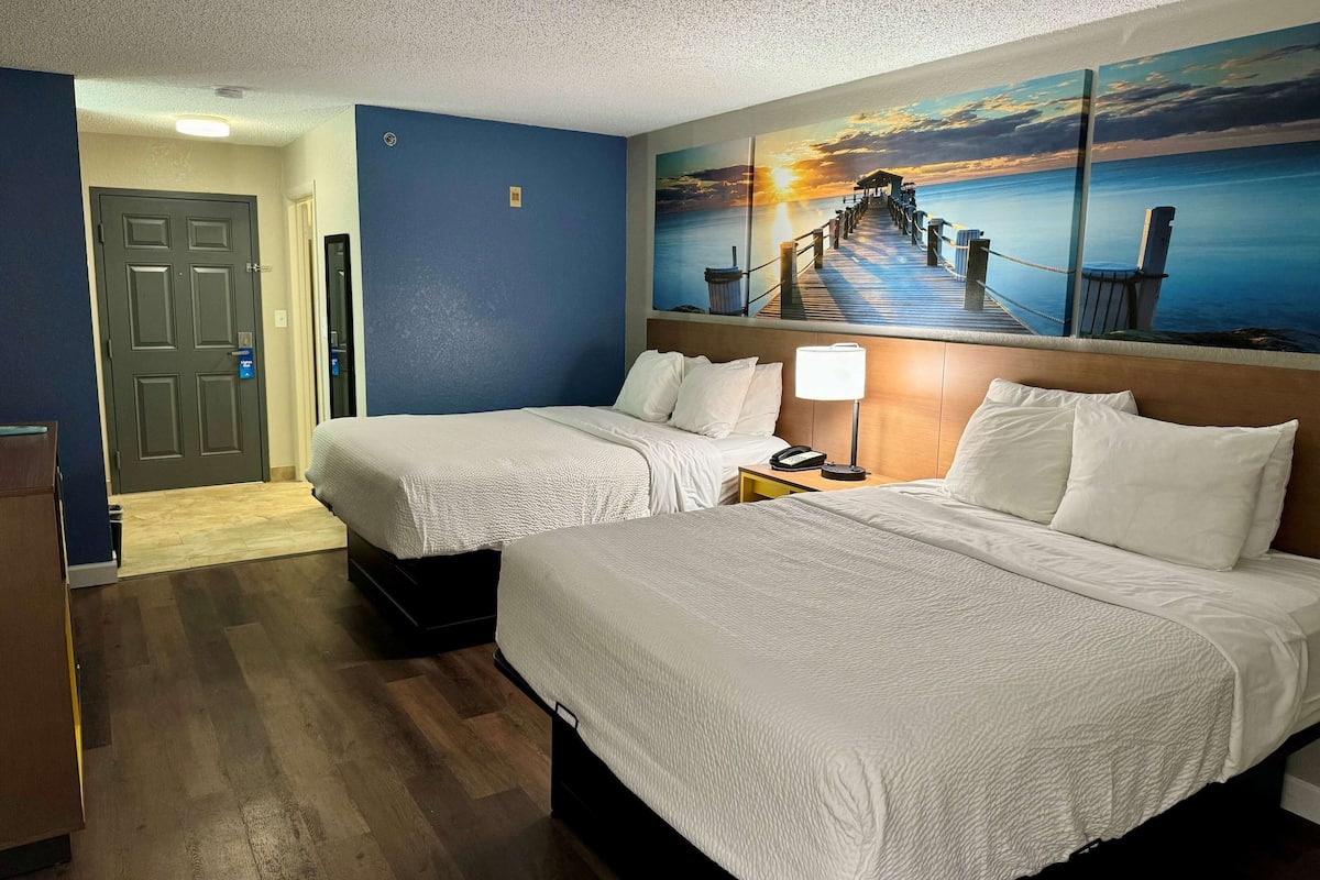 A hotel room with two beds, a painting of a sunset over water, and a wooden floor.