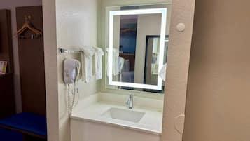 A hotel bathroom with a white sink, a mirror with a light, a hairdryer, and a towel rack.