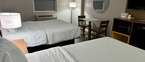 A hotel room with two beds, a desk, a chair, a TV, a lamp, and a microwave.