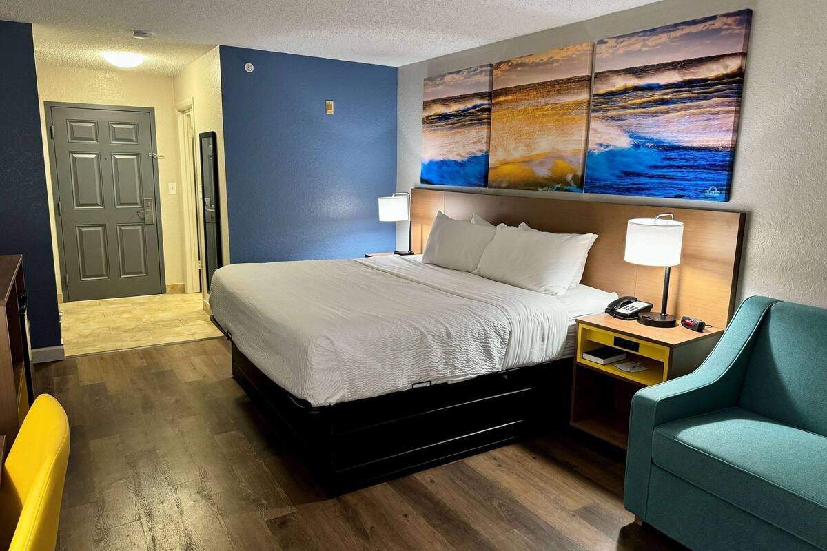 A hotel room with a bed, bedside tables, a chair, and artwork on the wall.