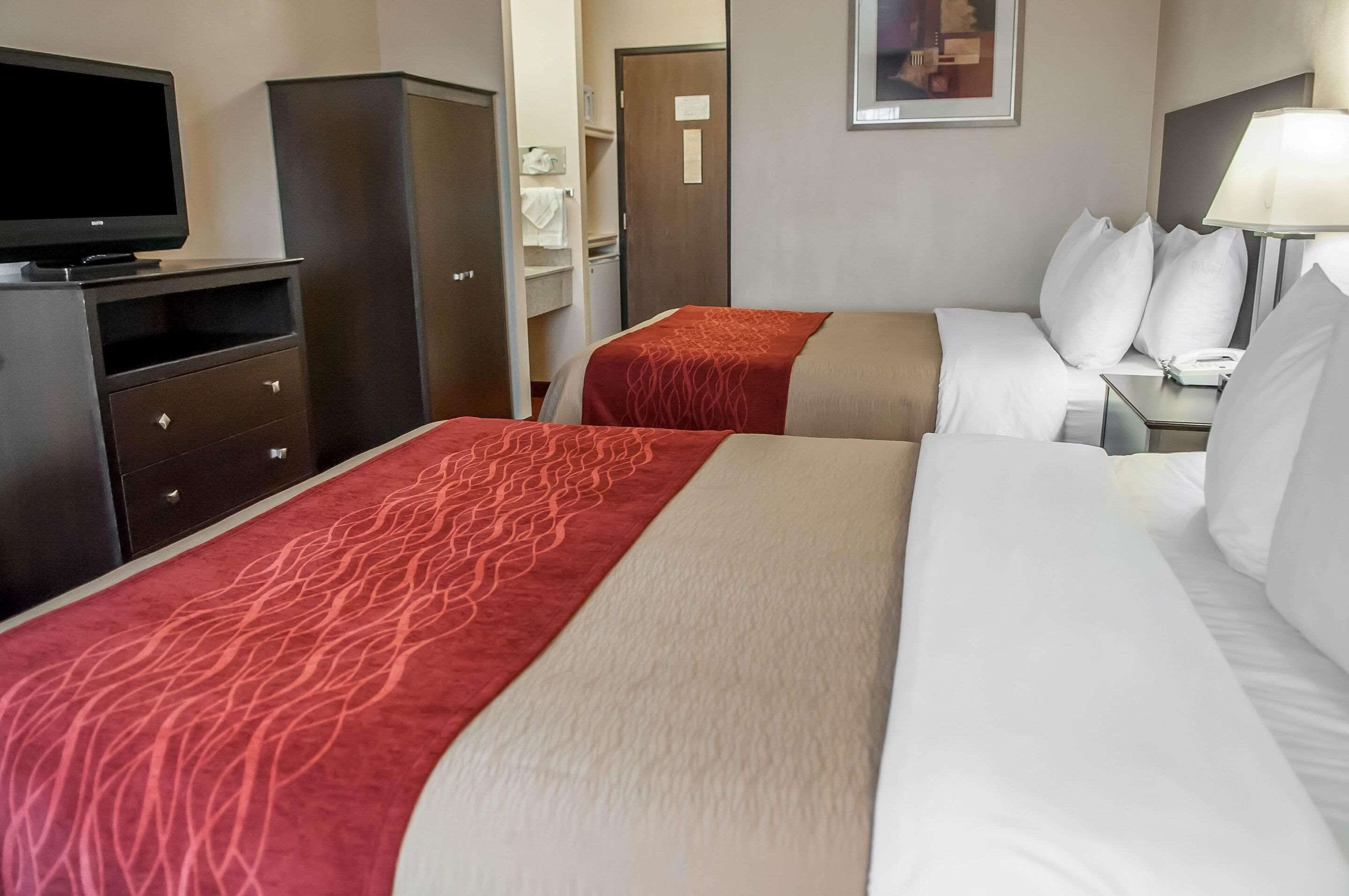 Hotellihuone, jossa on kaksi sänkyä, televisio, vaatekaappi ja työpöytä, jossa on lamppu.