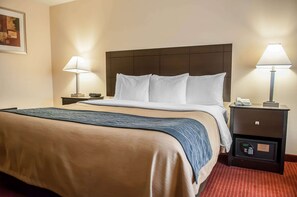 Una habitación de hotel con una cama grande, dos mesitas de noche con lámparas, una mesita auxiliar con teléfono y caja fuerte, y un cuadro enmarcado en la pared.
