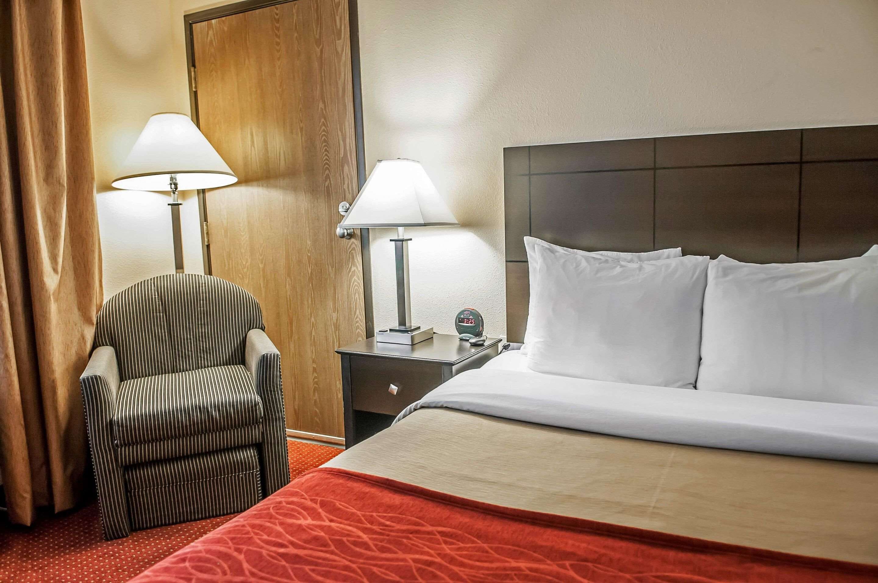 Una camera d'albergo con un letto, due lampade sui comodini, una sedia e un comodino con una sveglia.