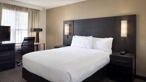 Habitación de hotel con una cama grande, un escritorio con silla, un televisor de pantalla plana y dos lámparas de noche.
