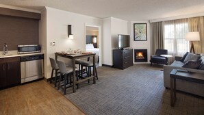 Una habitación de hotel moderna con cocina, comedor y sala de estar. Cuenta con un televisor de pantalla plana, chimenea y sofá.