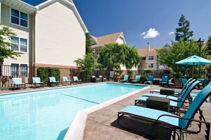 A swimming pool with lounge chairs and umbrellas, surrounded by buildings and trees.