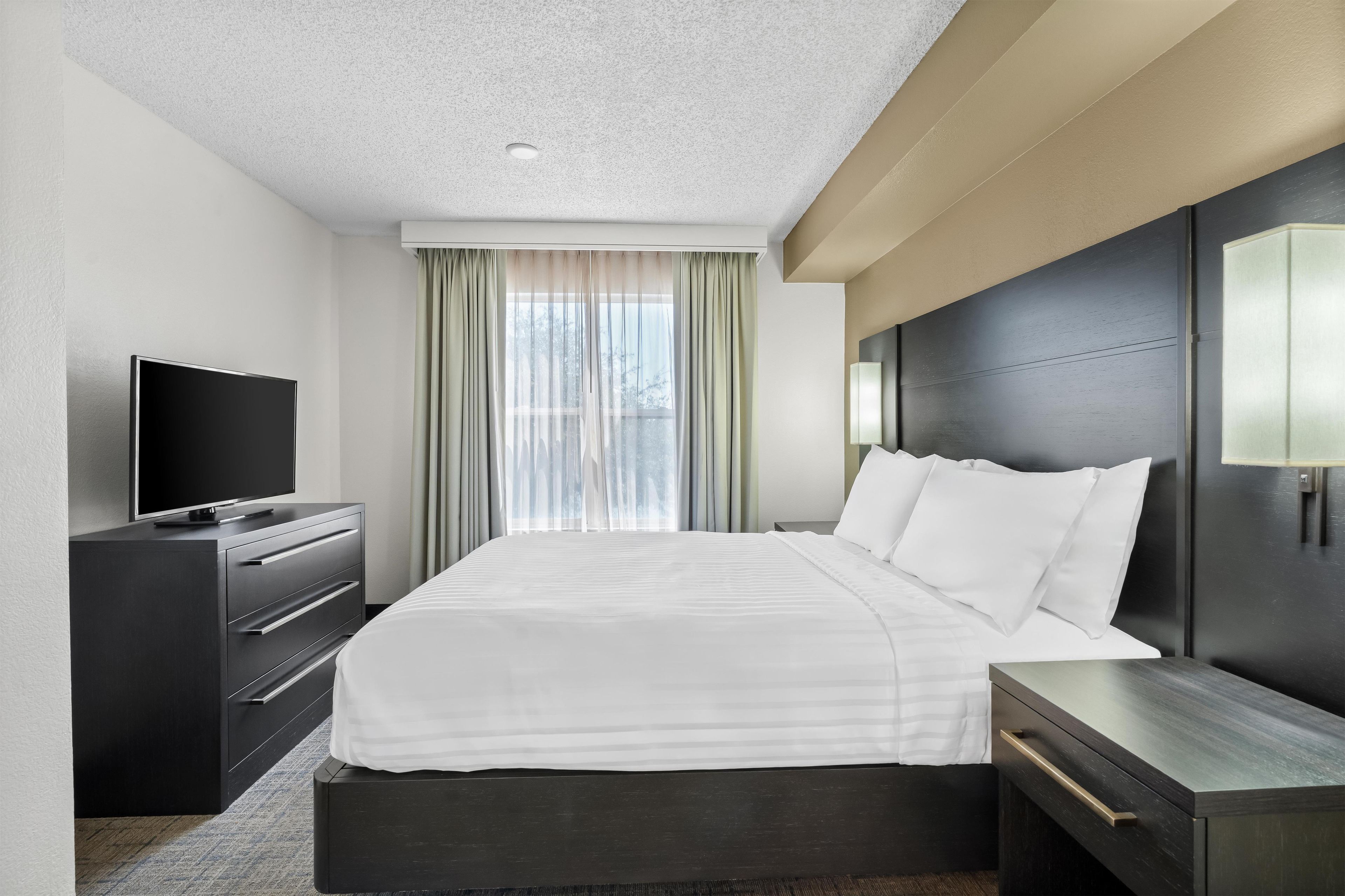 A hotel room with a bed, a TV, a desk, and a window with curtains.