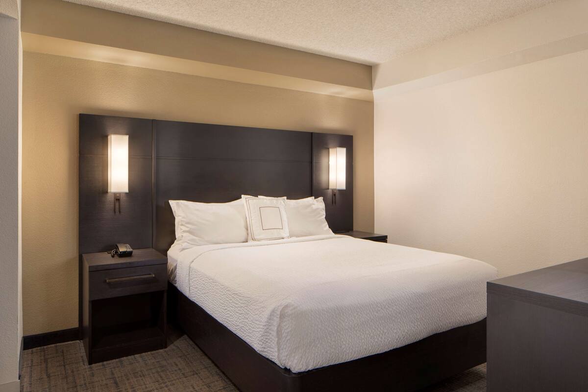 A neatly made bed with white linens, a dark headboard, and two bedside lamps.