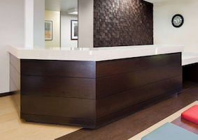 A reception desk with a dark wood finish, a white countertop, and a wall clock.