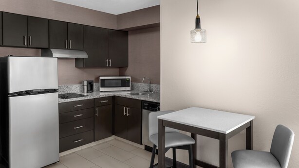A modern kitchen with dark cabinets, a stainless steel refrigerator, a microwave, and a small dining table with two chairs. - Residence Inn by Marriott Mystic Groton (Mystic)