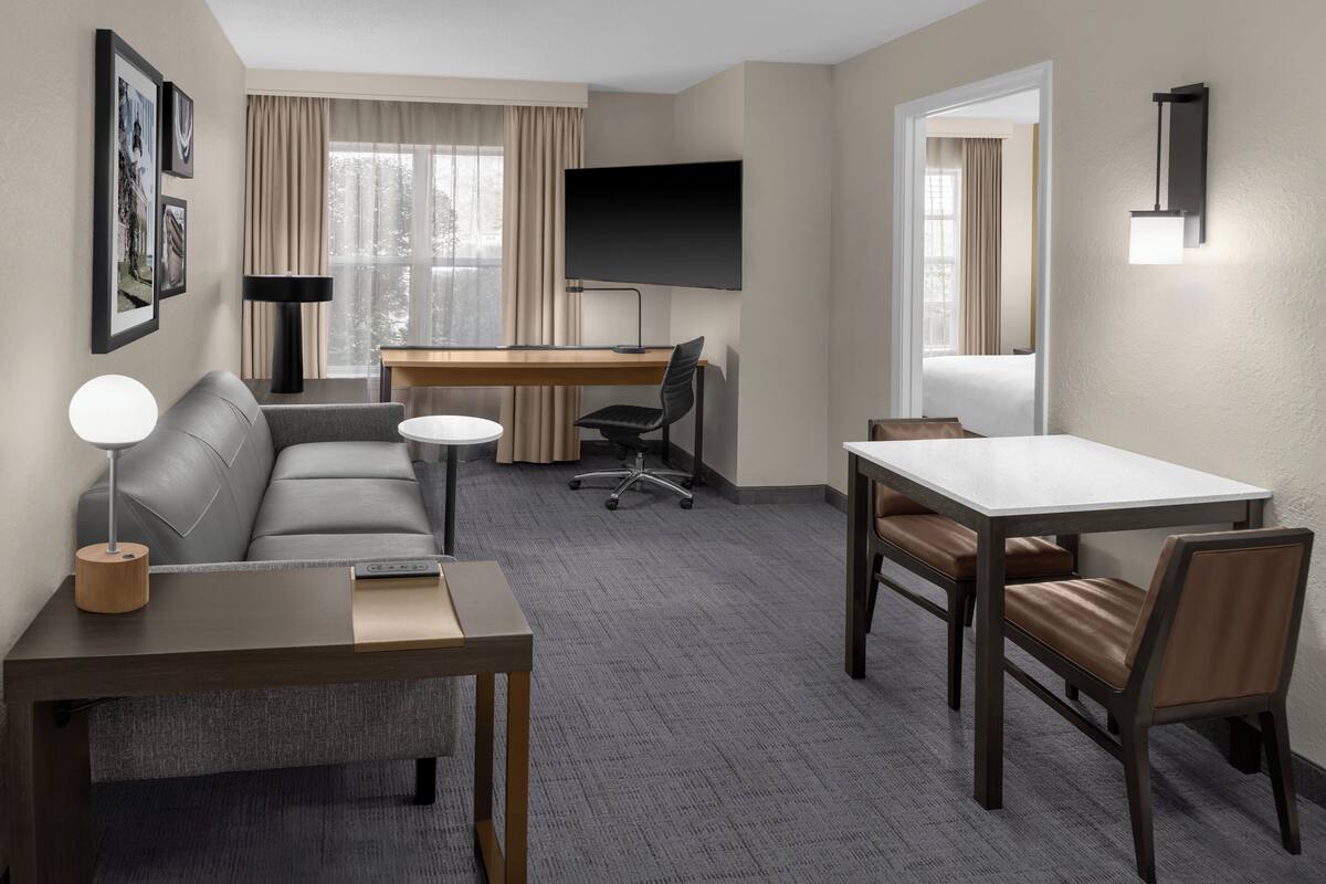 A hotel room with a sofa, a desk, a TV, a lamp, a table, and a chair.