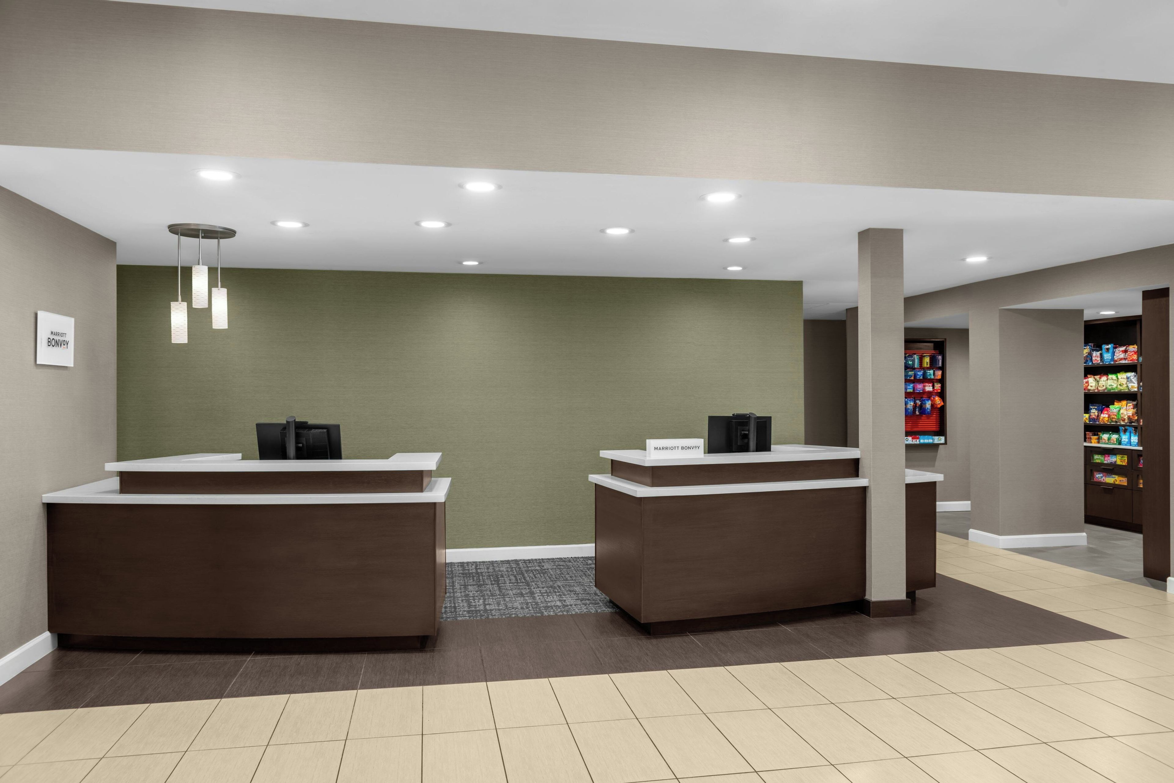 A hotel reception area with two reception desks, a green wall, and a vending machine in the background.