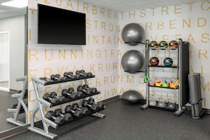 A gym with a wall-mounted TV, dumbbells, kettlebells, and a weight rack. - Residence Inn by Marriott Mystic Groton (Mystic)