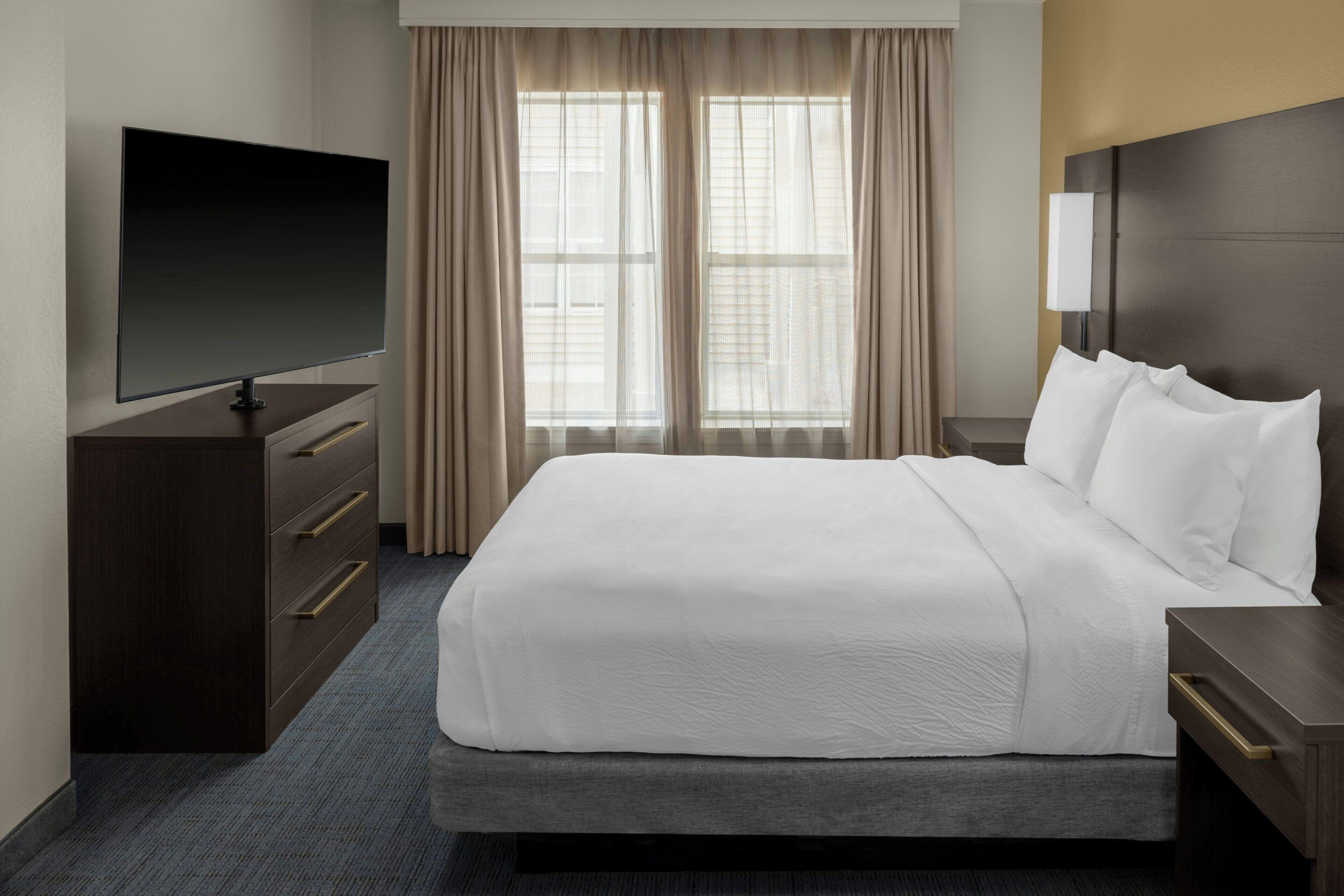 A hotel room with a large bed, a flat-screen TV, a dresser, and a nightstand.