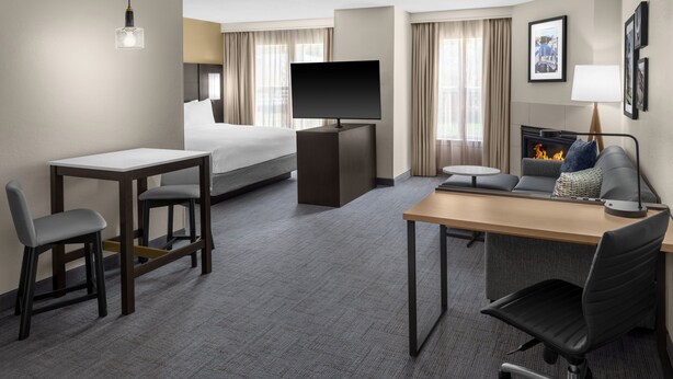 A hotel room with a bed, a desk with a chair, a television, a fireplace, and a sofa. - Residence Inn by Marriott Mystic Groton (Mystic)