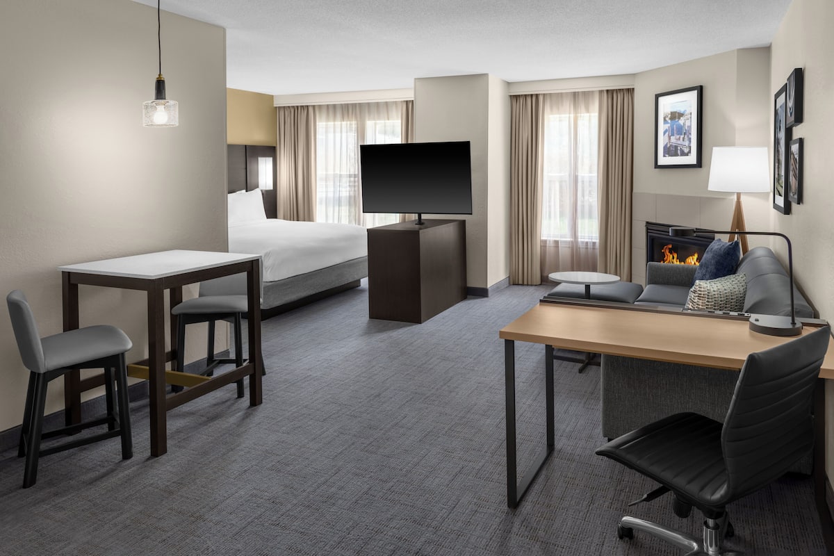 A hotel room with a bed, a desk with a chair, a television, a fireplace, and a sofa.