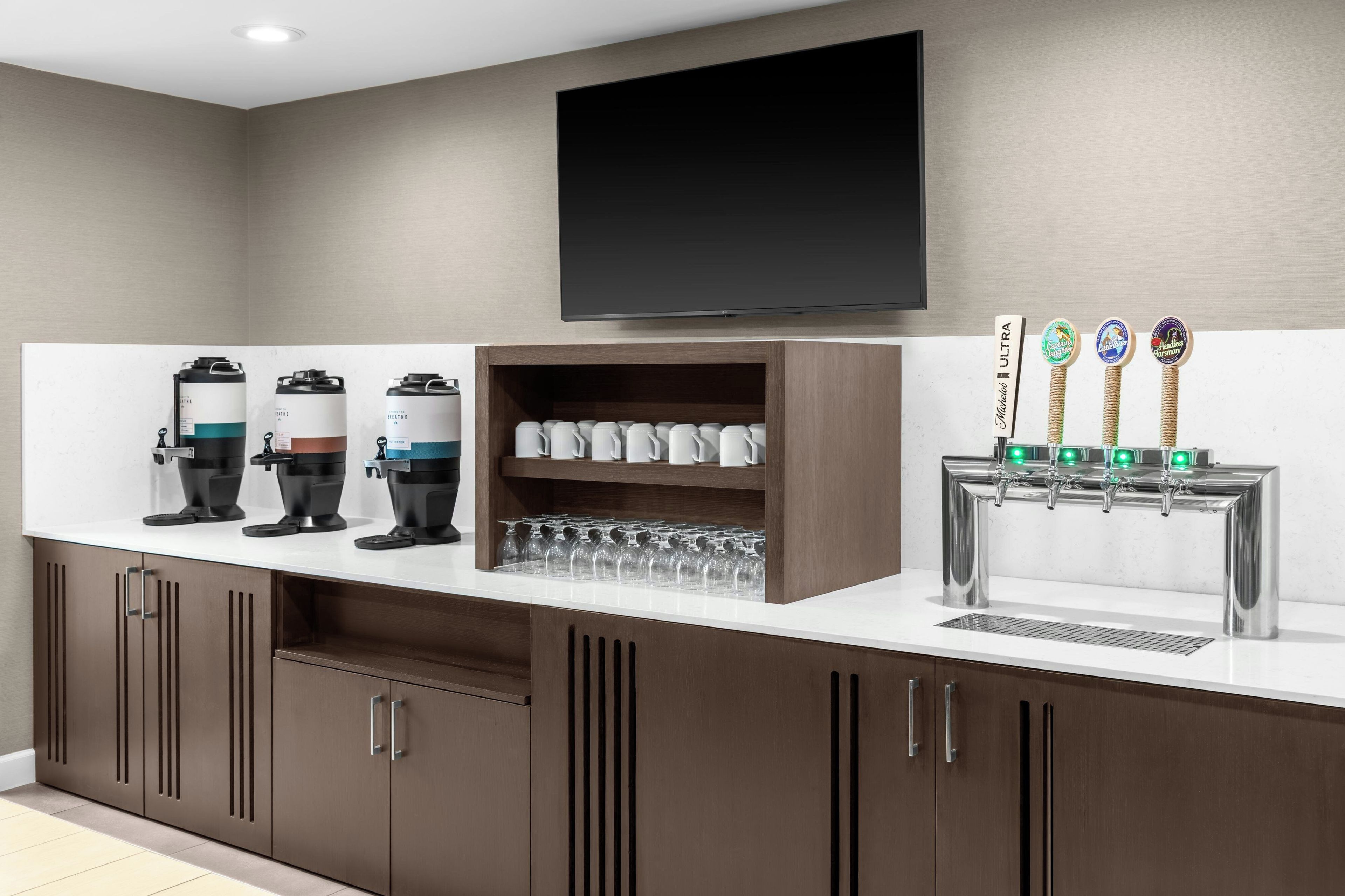 A modern bar area with a flat-screen TV, coffee machines, a glassware rack, and a beer tap station.