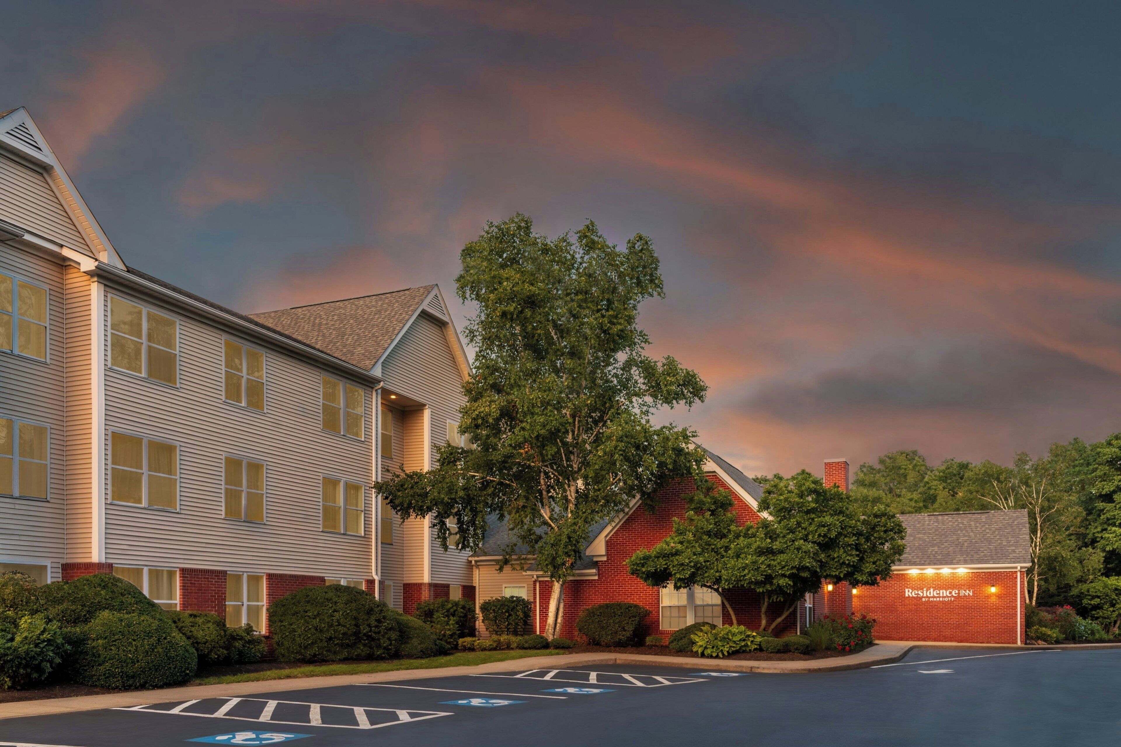 A hotel with a parking lot, a tree, and a building with a brick facade.