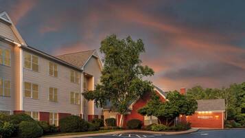 A hotel with a parking lot, a tree, and a building with a brick facade.