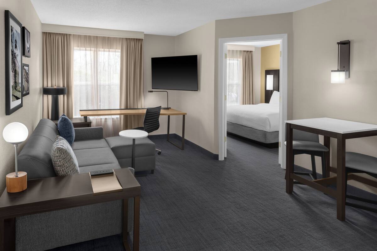 A hotel room with a sofa, a desk, a TV, a bed, and a small table.