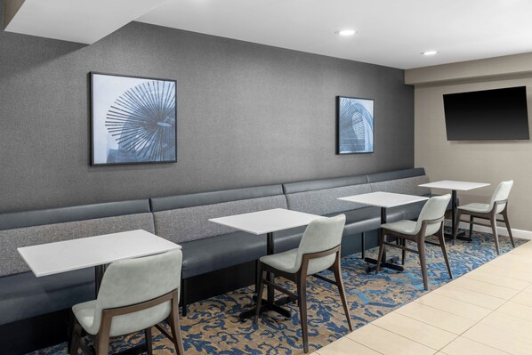 A modern hotel lobby with a grey upholstered bench, white tables, and chairs.