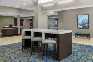 Un vestíbulo de hotel con una recepción, una zona de bar con taburetes y un área de estar con mesas y sillas.