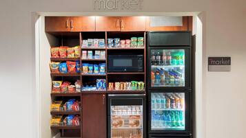 A compact kitchenette with a microwave, refrigerator, and pantry stocked with snacks and beverages.