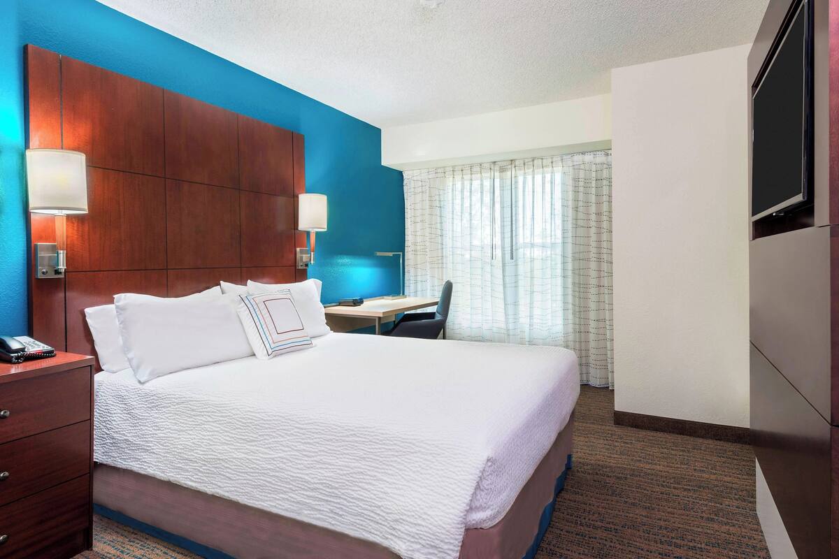A hotel room with a large bed, a desk, and a TV.