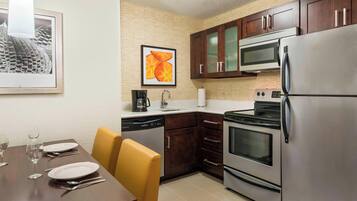 A modern kitchen with stainless steel appliances, wooden cabinets, and a dining area with yellow chairs.