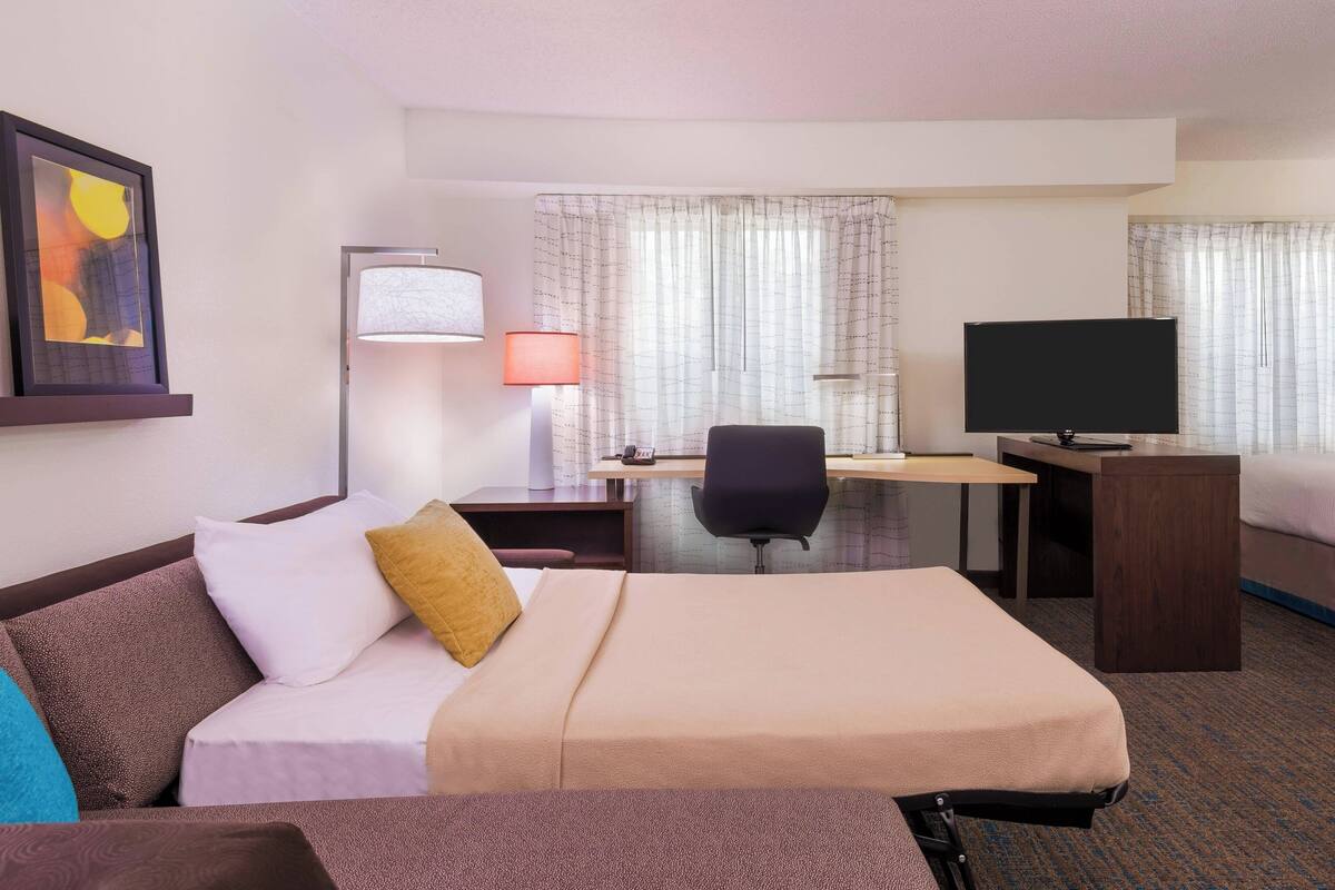 A hotel room with a bed, a desk, a chair, a television, and a lamp.