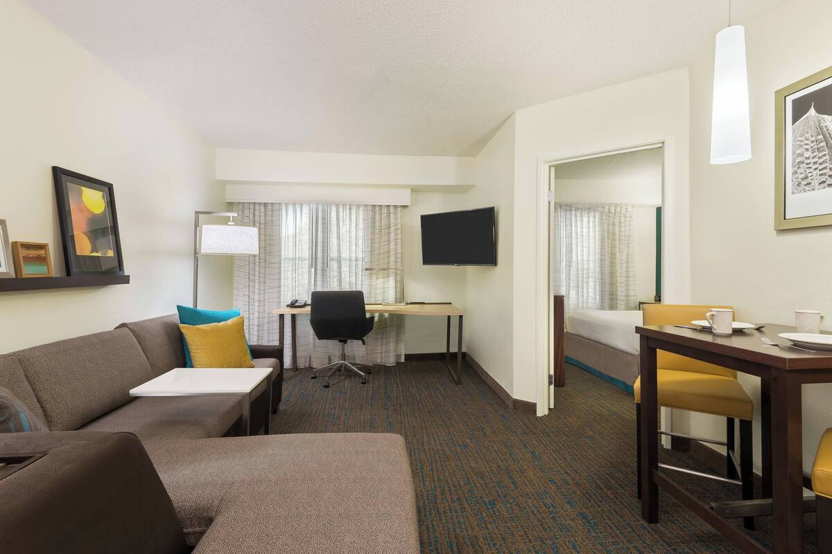 A hotel room with a sofa, a desk, a chair, a bed, and a television.
