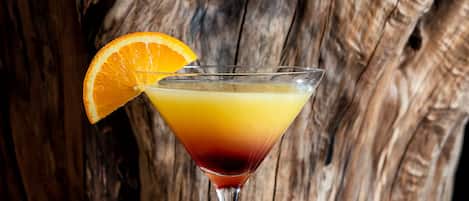A cocktail glass with a slice of orange on the rim, placed on a wooden surface with a rough texture.