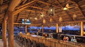 A bar area with wooden furniture and hanging lights, overlooking a pool and beach area. - Lido Beach Resort (Sarasota)