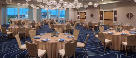 A large conference room with round tables, beige chairs, and a blue carpet.