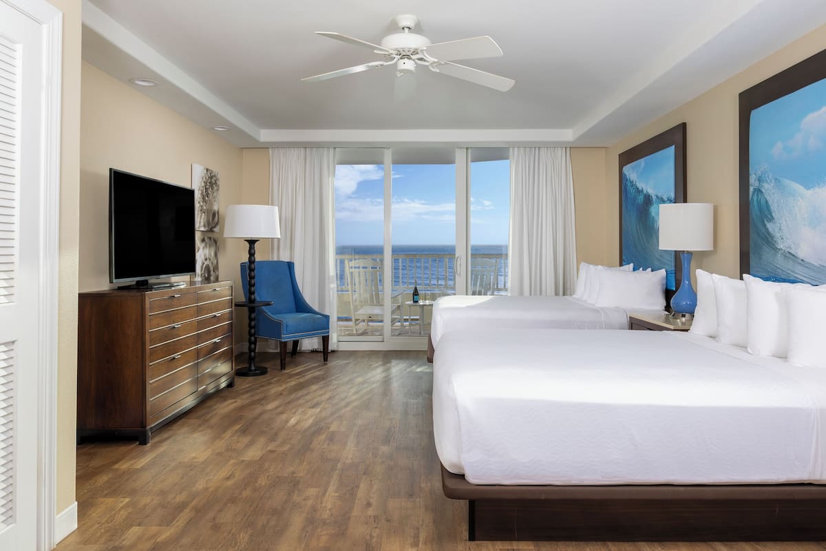 A hotel room with two beds, a TV, a dresser, a chair, and a balcony with a view of the ocean.