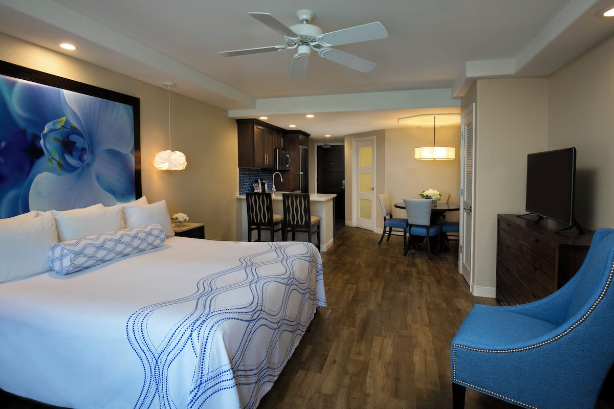 A hotel room with a large bed, a desk, a chair, a television, and a ceiling fan.