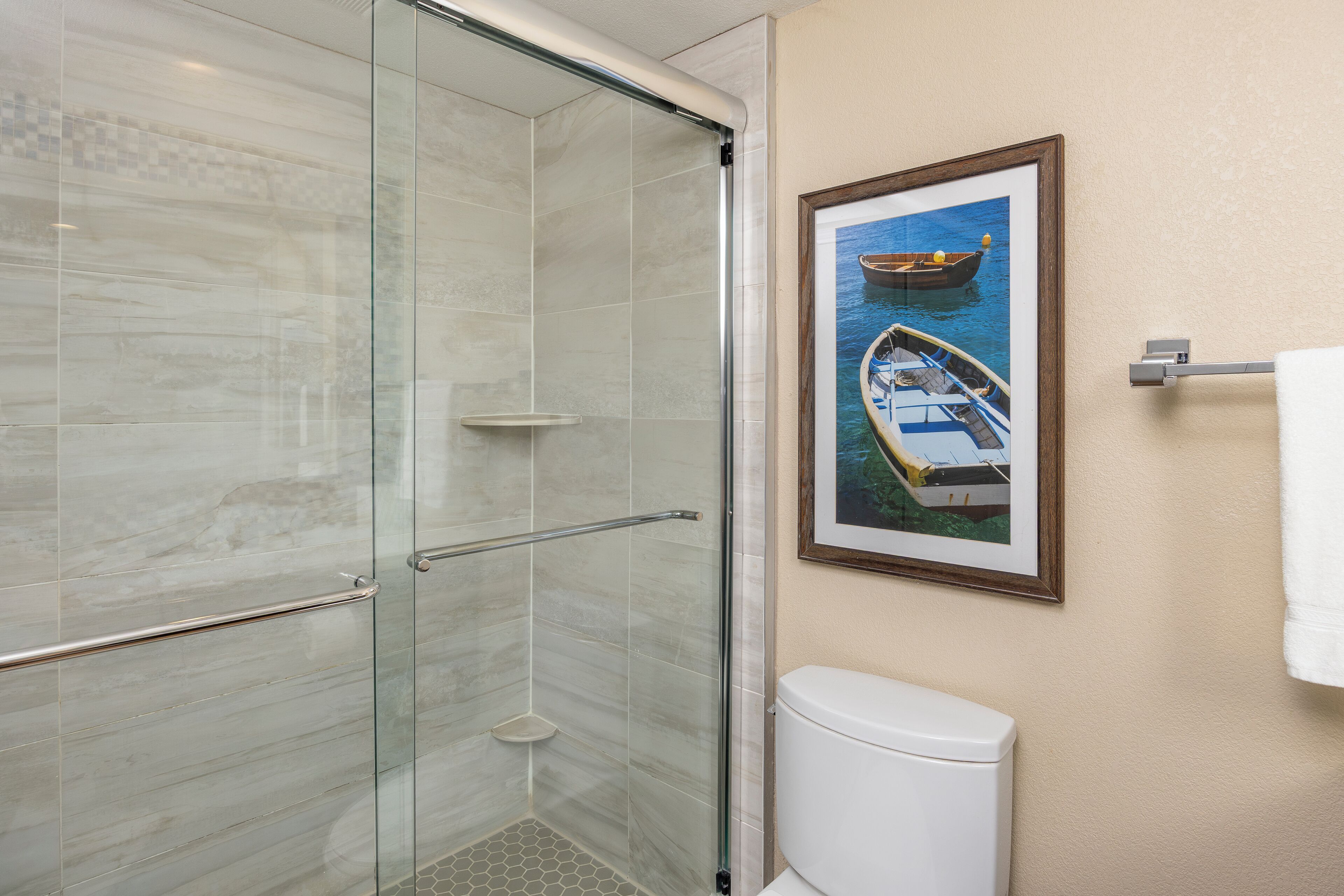 Un baño con cabina de ducha de vidrio, un inodoro y un cuadro con una imagen de un barco en el agua.