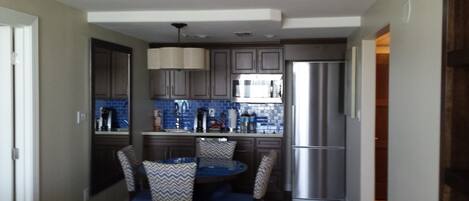 A compact kitchen with modern appliances, a dining area with blue chairs, and a small table.