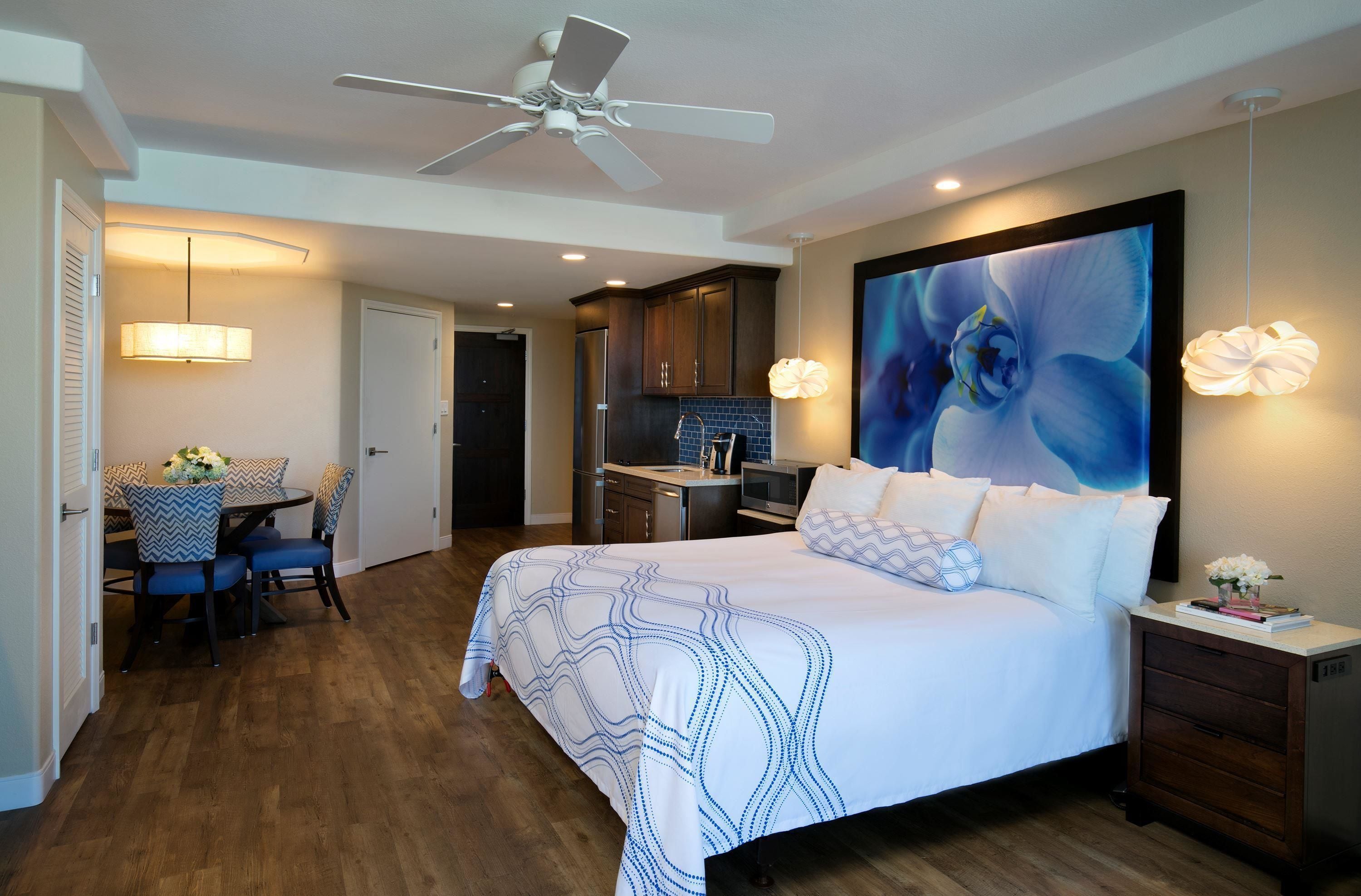 A modern hotel room with a large bed, a dining area, and a kitchen.