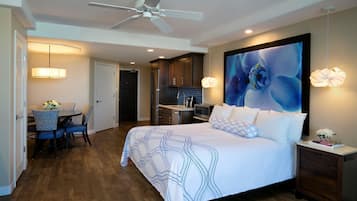 A modern hotel room with a large bed, a dining area, and a kitchen.